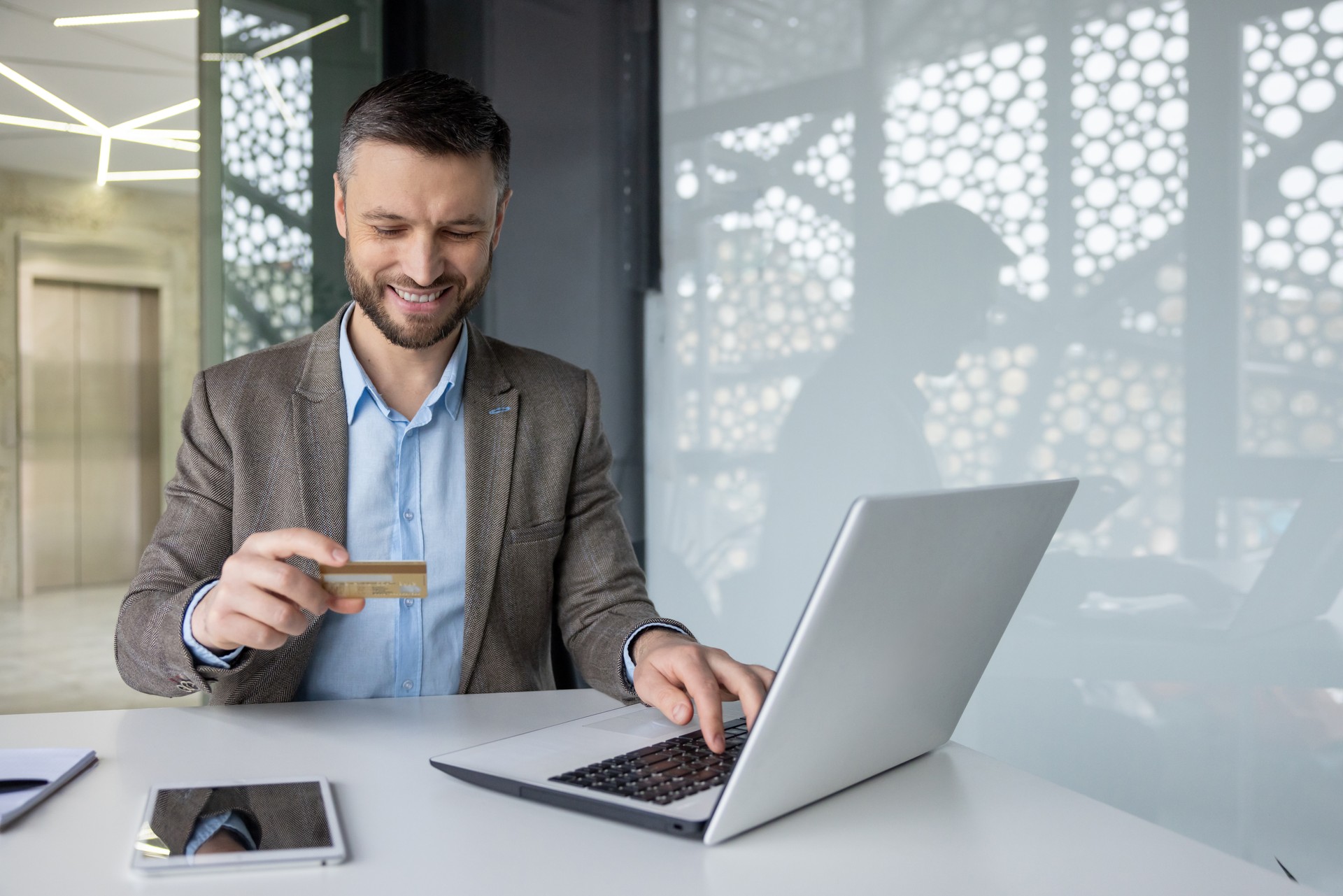 Businessman making online payment with credit card on laptop at modern office